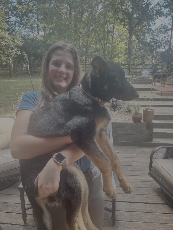 A volunteer holding a German Shepherd in her arms outdoors