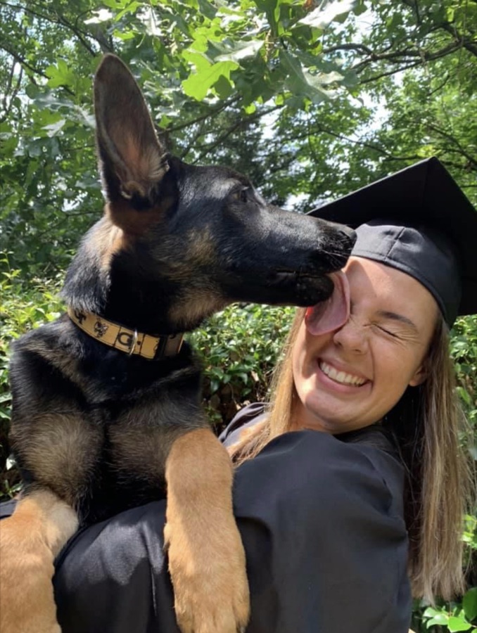 A volunteer in graduation cap and gown with her German Shepherd